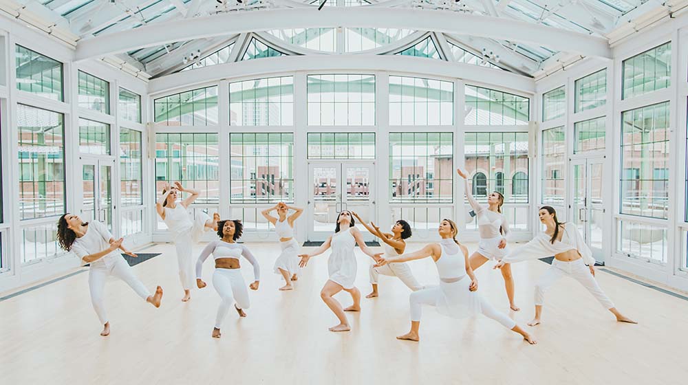 Sandra Kaufmann, sitting against the mirrored wall, watches dance students as they dance near her.