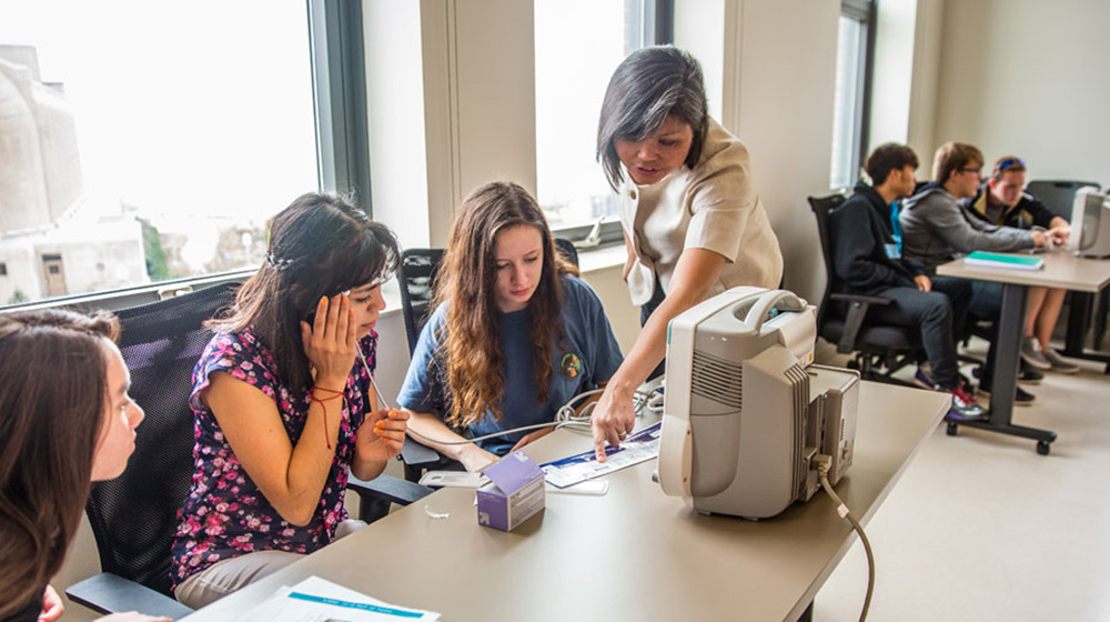 An engineering professor interacts with three attentive students gathered a a table in a classroom.