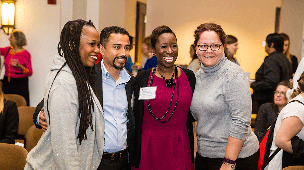 Four individuals smiling and posing together for a photograph at a lively event, capturing a moment of joy and camaraderie.