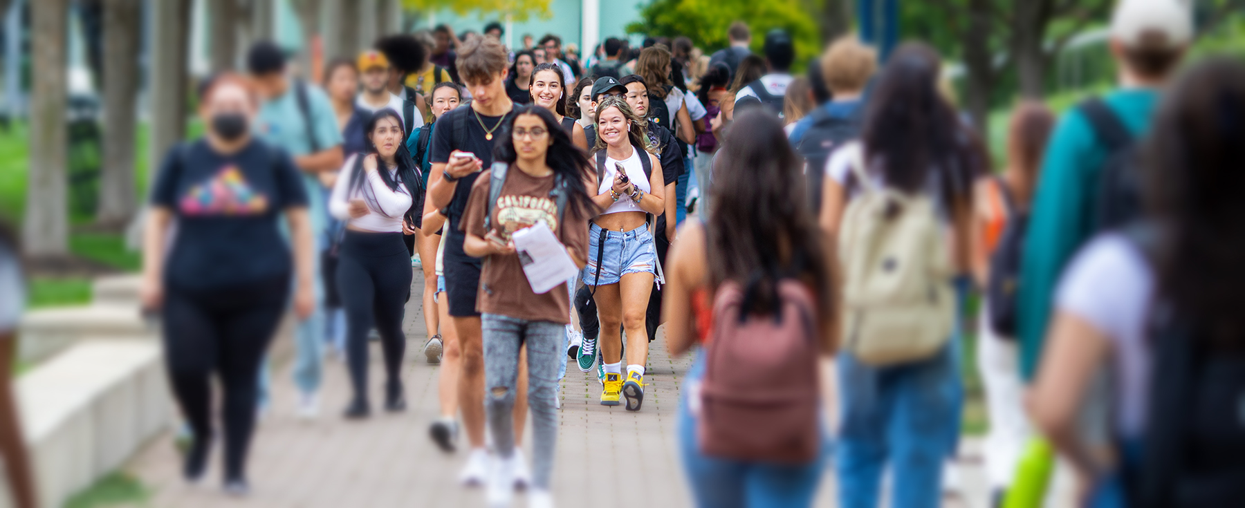 Many students walking on campus and two young women in the center talking.