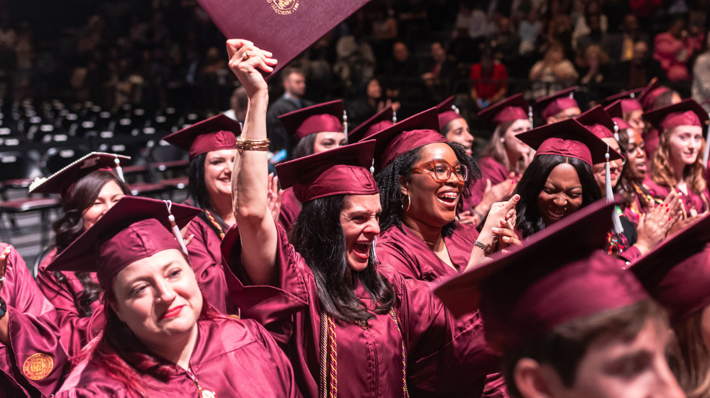 Loyola SCPS graduate Jackie Gilbert holds up diploma in cap and gown